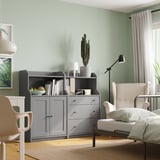 Modern light grey living space with grey HAUGA furniture, a large cactus plant, and a cozy armchair near a window with sheer curtains.