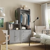 Beautiful bedroom with HAUGA gray storage unit, white curtains, and cozy chair. Clothes hang neatly, decor includes a cactus.