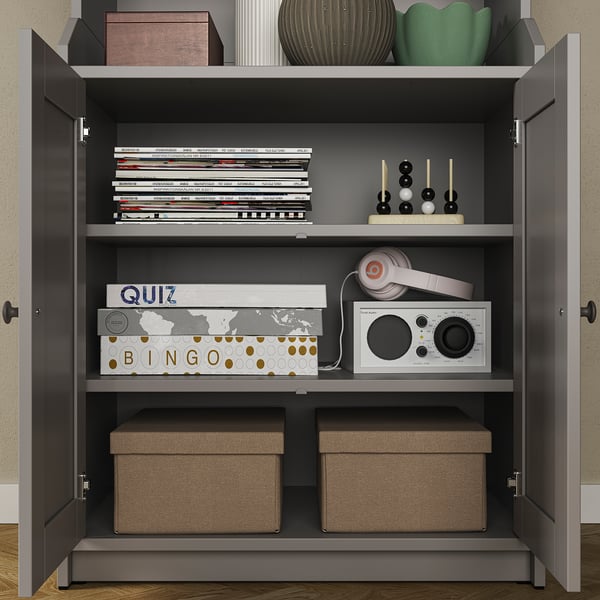 A gray HAUGA storage cabinet with multiple compartments, storing books, games, headphones, and more.