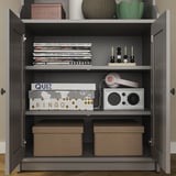A gray HAUGA storage cabinet with multiple compartments, storing books, games, headphones, and more.