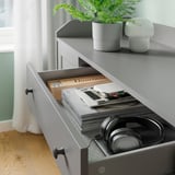 Gray HAUGA drawer with open compartment, holding books, headphones, notebooks, and stationery items.