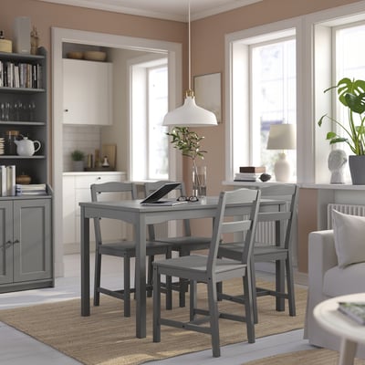 Cozy dining area with HAUGA table, vase, laptop on beige rug, kitchen in background.