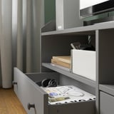 Gray HAUGA tv stand with drawers, headphones, books, remotes, and magazine on open drawer.
