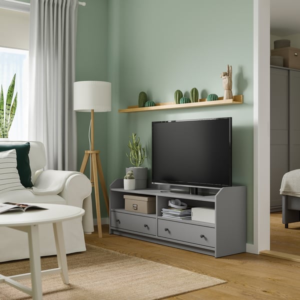 Cozy living room with green walls, white couch, grey tv stand holding flat screen tv, plants, and wooden floor.