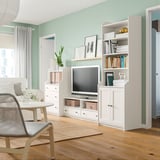 Living room with white HAUGA furniture: tv unit, bookcase & chest. Tv on, green walls, light wood floor.
