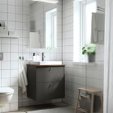 Modern bathroom with HAVBÄCK dark grey vanity. Wood top, white sink, large mirror. Towel hangs left, stool right.