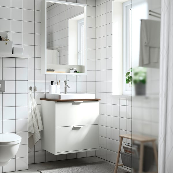 Modern white HAVBÄCK bathroom setup. Vanity fits under large mirror, with a sink, countertop, and towel. Room clean lines and minimalist design.