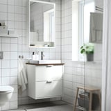 Modern white HAVBÄCK bathroom setup. Vanity fits under large mirror, with a sink, countertop, and towel. Room clean lines and minimalist design.