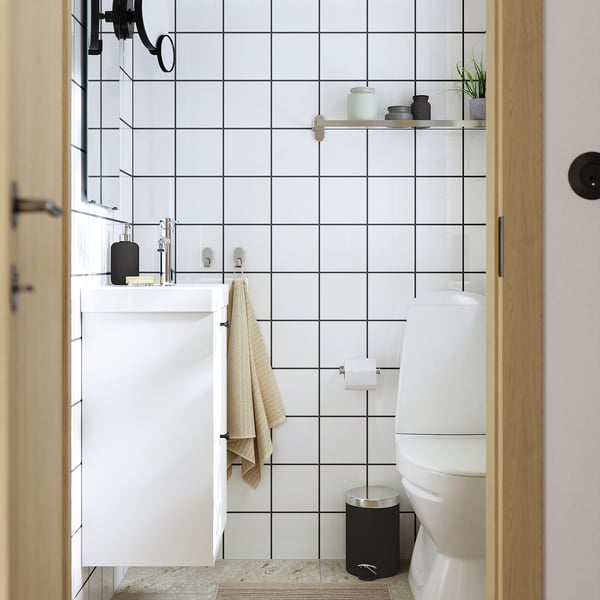 Modern bathroom: white tiled walls, compact white cabinet, black accents, sleek ceramics, minimalist decor.