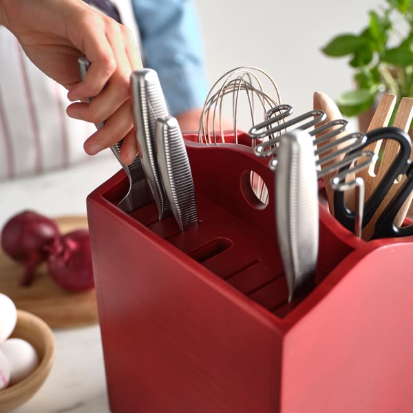 Person holding a knife from a red HAVSMAL wooden knife block, which organizes knives and kitchen tools neatly on the countertop.