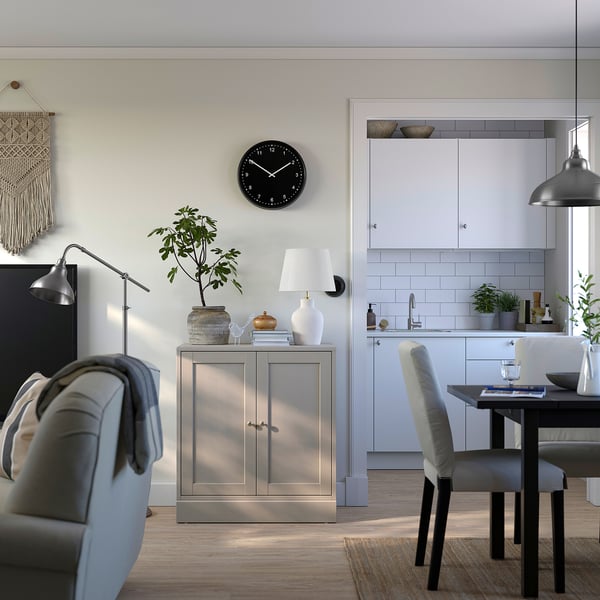Modern living room featuring a rustic grey HAVSTA cabinet, a black wall clock, cushioned chairs, and wooden floors.