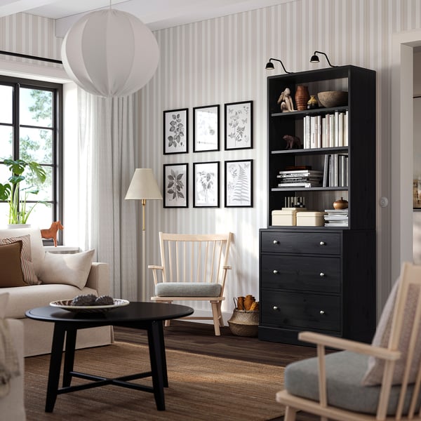 Modern living room with black bookshelf, rocker chair, and large window.