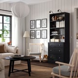 Modern living room with black bookshelf, rocker chair, and large window.