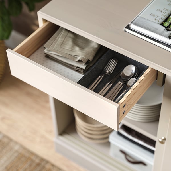 Open drawer shows cutlery, folded napkins in light wooden cabinet.