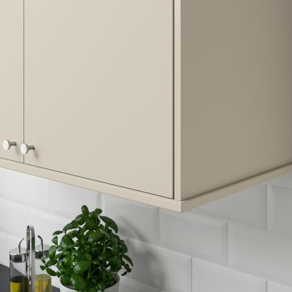 Beige kitchen cabinet with round knobs, hiding lighting and cords, against white tiles, and a potted plant below.