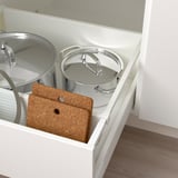 This image shows a white cabinet holding two covered pots and a rectangular cork trivet. Cork is natural and variations in color are normal.