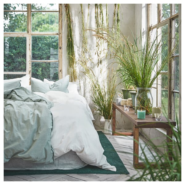 Serene bedroom with large windows, light bedding, grassy decor, and candle.