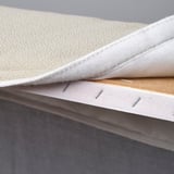 Close-up of a divan beds corner displaying soft, removable mattress cover with stitching and wooden slats underneath.