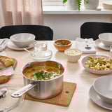 Soup table set with black chairs, wooden trivet, bowls, bread, and toppings.