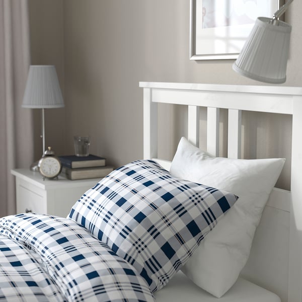 Cozy bed with blue plaid, white pillows, bedside tables with lamps, alarm clock, and books.
