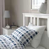 Cozy bedroom corner with wooden bed, blue checkered bedspread, two bedside lamps, and under-bed storage.