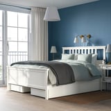 HEMNES white bed with storage against blue wall, brass lights, large window.