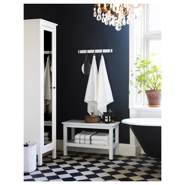 Modern black and white bathroom with HEMNES cabinet, hooks, and bench. Dark walls contrast with checkered floor, white fixtures, and plants.