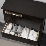 Dark wood chest with open drawers, neatly storing folded clothes. Dividers organize items visually.
