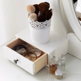 White vanity with open drawer showing jewelry boxes and ring holder, perfumes, and makeup brush holder on top.