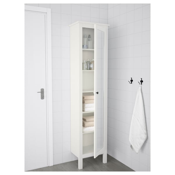 White bathroom cabinet with mirror, glass doors, towels & toiletries, black hooks.