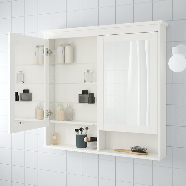White bathroom cabinet, open with glass shelves holding bottles, jars, makeup brushes, and a hairbrush.