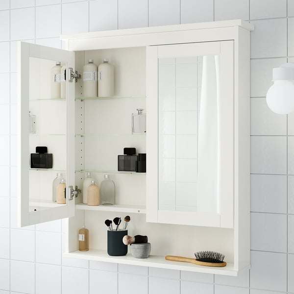 White wall-mounted bathroom mirror cabinet with adjustable glass shelves, storing toiletries and makeup items.