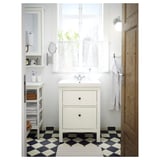 Modern white bathroom with a white HEMNES vanity, black and white checkerboard floor, light grey towels, and a window with sheer curtains.