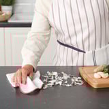 Person wiping kitchen surface with red-edged cloth.
