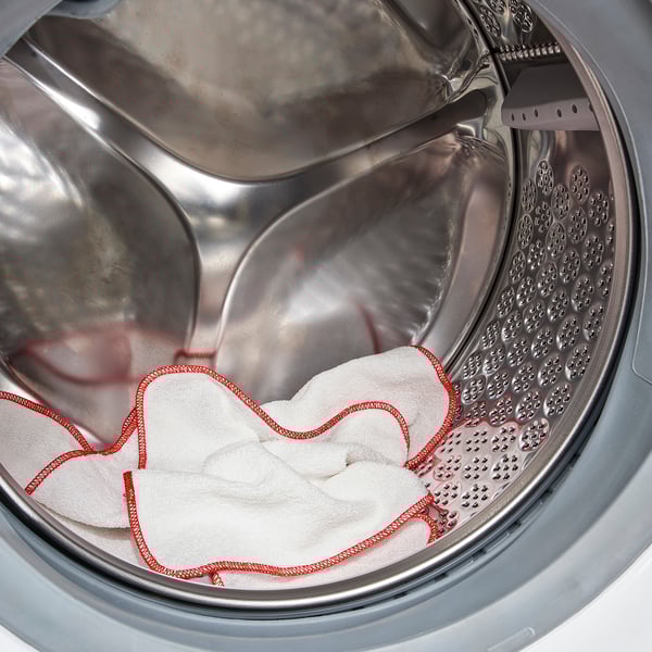 A silver drum washing machine with white towels and red trim inside, ready for a wash.