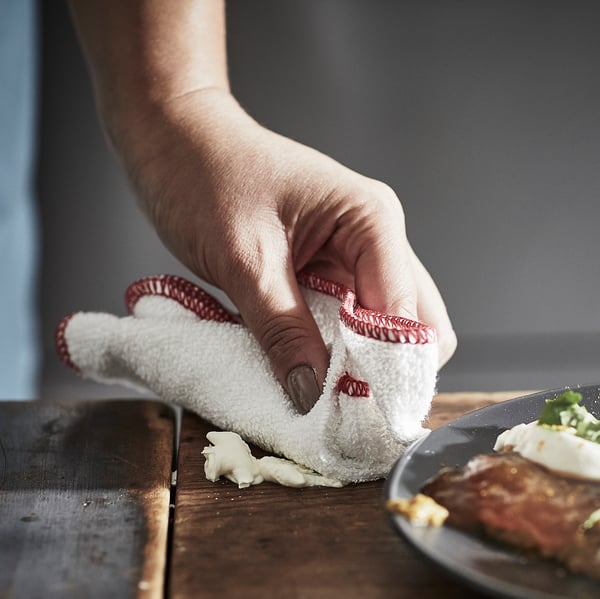Person cleaning surface with white red-edged cloth near plate.