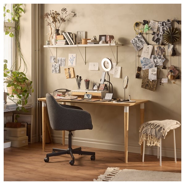 Home office setup with wooden desk, grey chair, and wall shelves; decorative with plants and art.