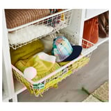 A white wire HJÄLPA basket holding folded clothes and a baseball cap, neatly organized on a shelf.