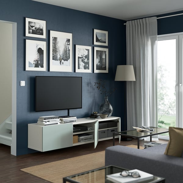 Modern living room with dark blue walls, featuring a tv on a white stand, surrounded by framed pictures, with a large window letting in natural light.