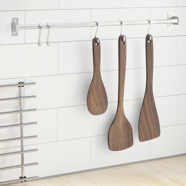 Wooden utensils hang on hooks against white tiles, contrasting with metal tool rack.