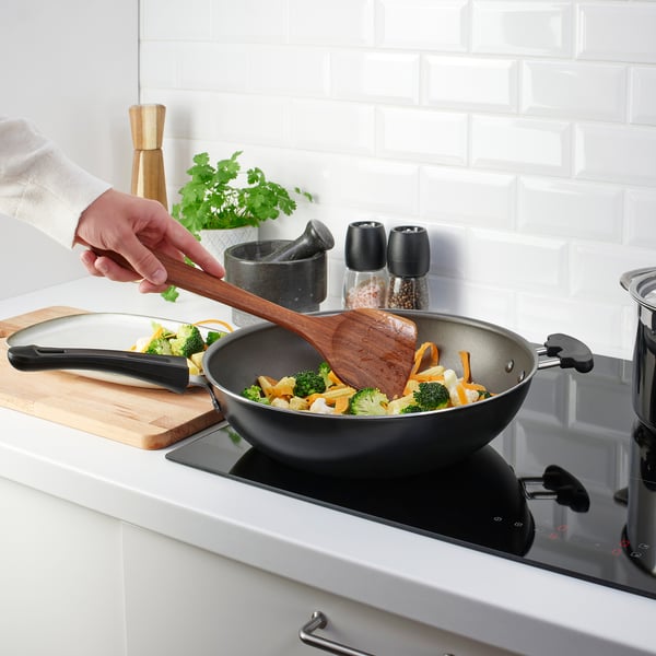 Person cooks vegetables in pan using wooden spatula in modern kitchen.
