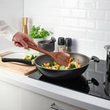 Person cooks vegetables in pan using wooden spatula in modern kitchen.