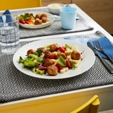 A meal featuring chicken meatballs, salad, and a beverage on a table with blue and white place settings.