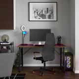 Gaming desk with red accents, dual monitor support, headphone hook, and ring light. Grey adjustable chair, pc with colorful lights.