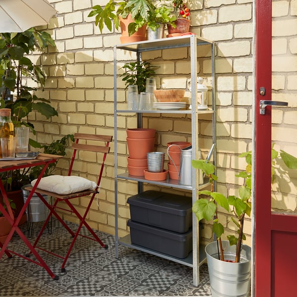 Metal outdoor shelf with red accents and plants against brick wall.
