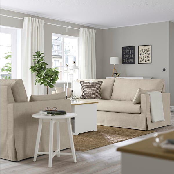 Modern living room with HYLTARP beige sofa, photo frames, white rug, side table, and lamp.