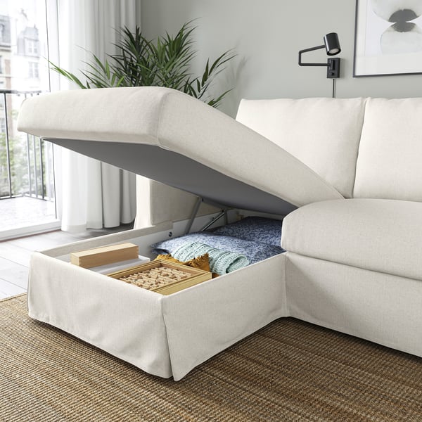 A modern cream sofa with a lift-up chaise longue revealing storage space holding blankets and board games.