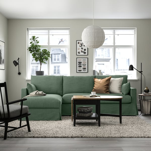 A stylish living room with a green HYLTARP sectional sofa, a coffee table, a black armchair, and a large window.