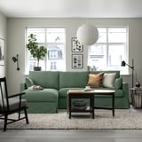 A stylish living room with a green HYLTARP sectional sofa, a coffee table, a black armchair, and a large window.