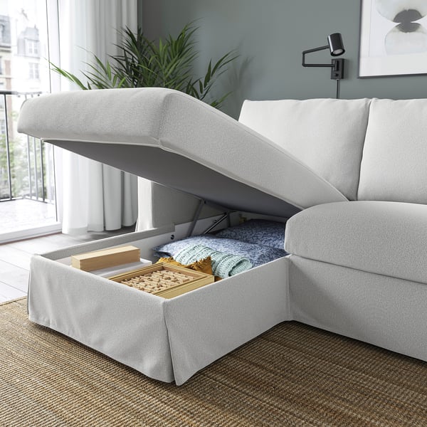 A modern sofa with a lift-up chaise longue revealing storage space with blankets and a board game inside.